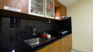 A kitchen with a black countertop, stainless steel sink, and wooden cabinets. - RedDoorz Plus @ Setiabudi Tengah (Jakarta)
