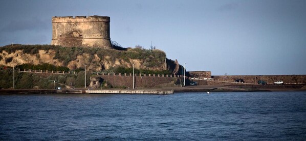A coastal fortification with a prominent tower, a fortified wall, and a pier extending into the water. - Hotel Al Gabbiano (Bosa)