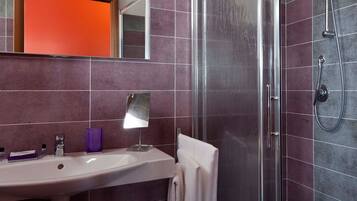 A bathroom with a sink, mirror, hairdryer, and shower.