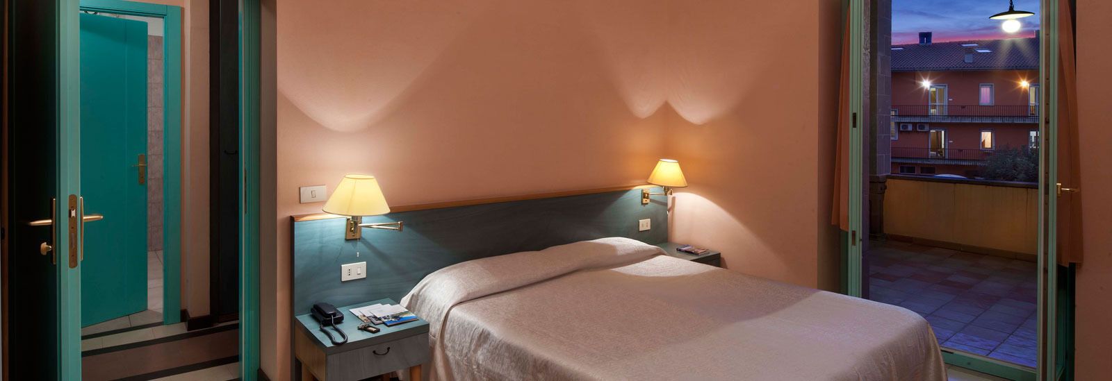 Habitación de hotel con cama, dos mesitas de noche y vistas al balcón exterior.