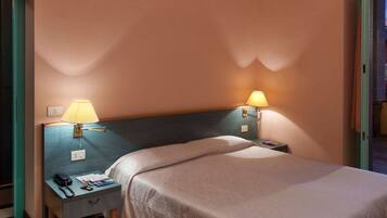Habitación de hotel con cama, dos mesitas de noche y vistas al balcón exterior.