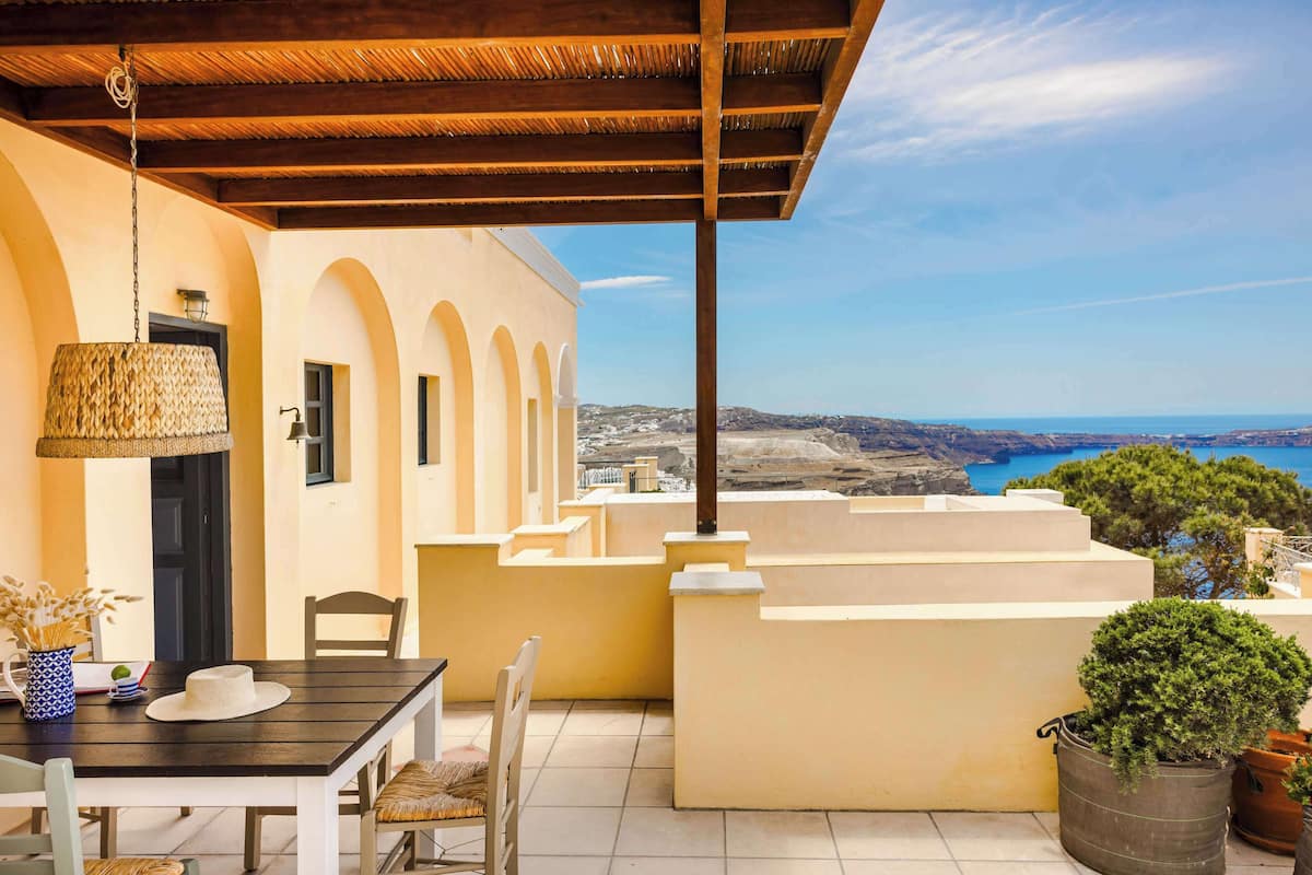 A terrace with a table and chairs, a hanging light fixture, and a view of the sea.