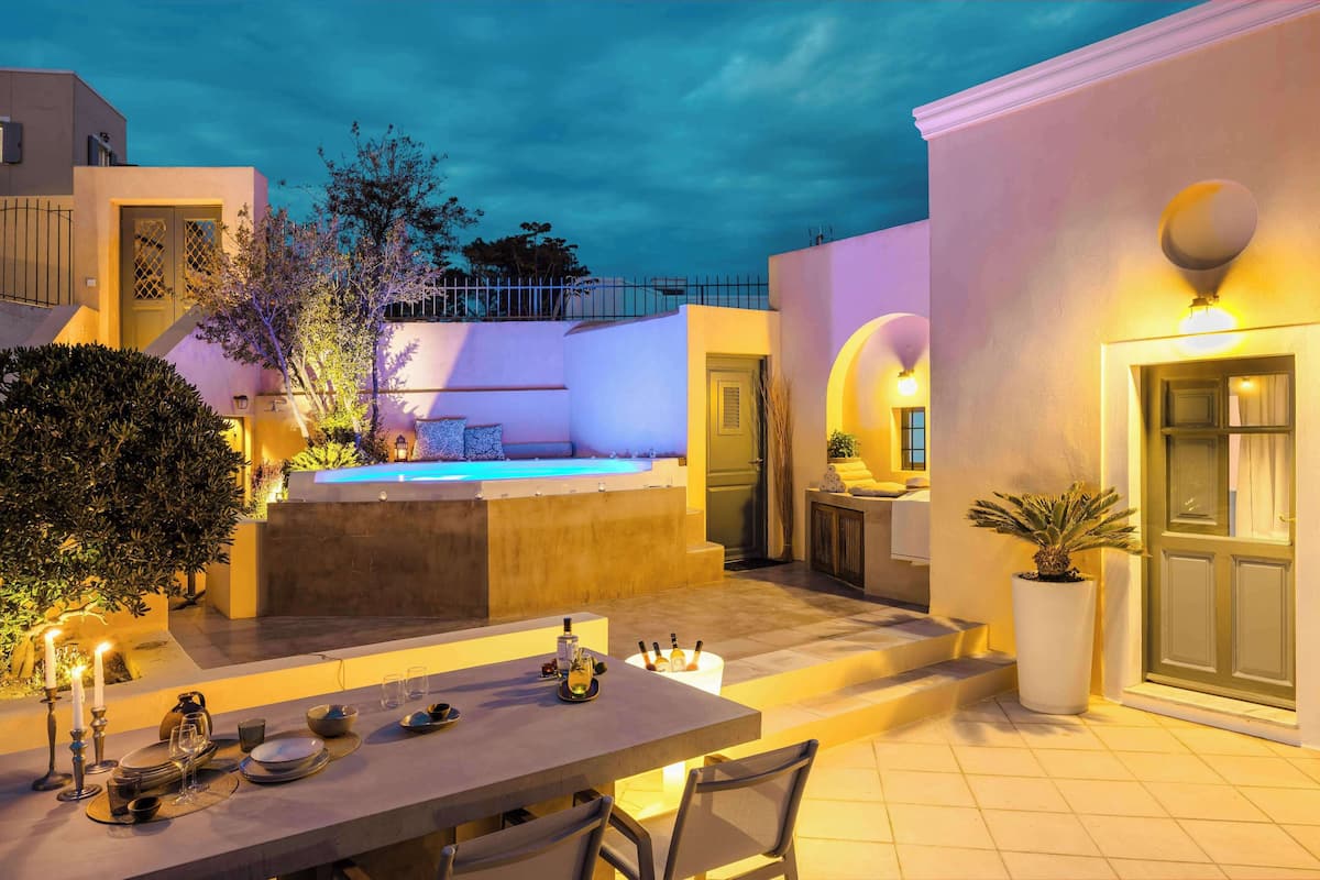 An outdoor dining area with a pool, a table set for two, and a staircase leading to a second level.