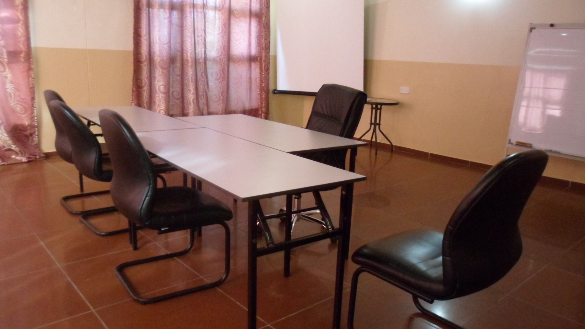 Une salle de conférence équipée d’une longue table, de quatre chaises, d’un tableau blanc et d’un écran de projection.