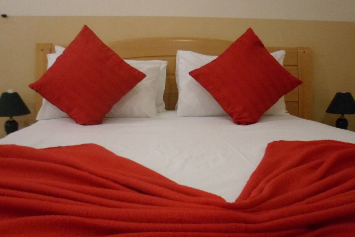Un lit recouvert d’une couverture rouge et agrémenté de deux oreillers rouges, avec deux lampes noires de chaque côté.