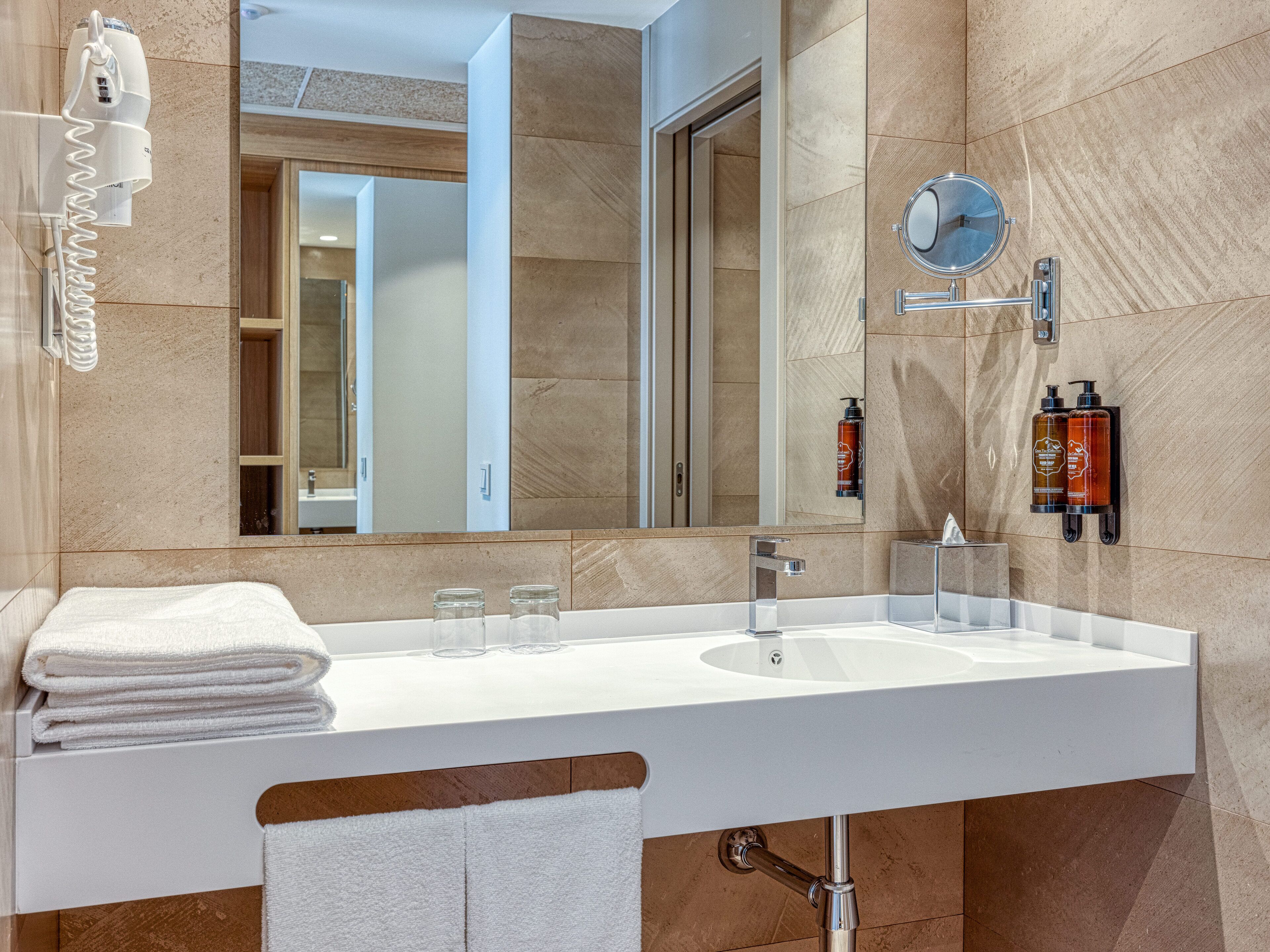 A modern bathroom with a large mirror, a white sink, and a towel rack.