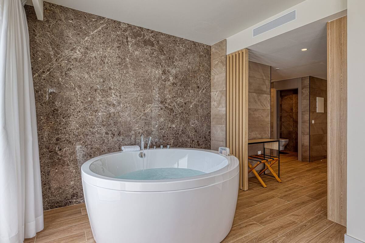 Une salle de bain moderne avec une grande baignoire ronde, un plancher en bois et un mur en marbre.