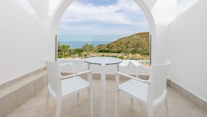 Een balkon met een witte tafel en stoelen, met uitzicht op zee en heuvels.