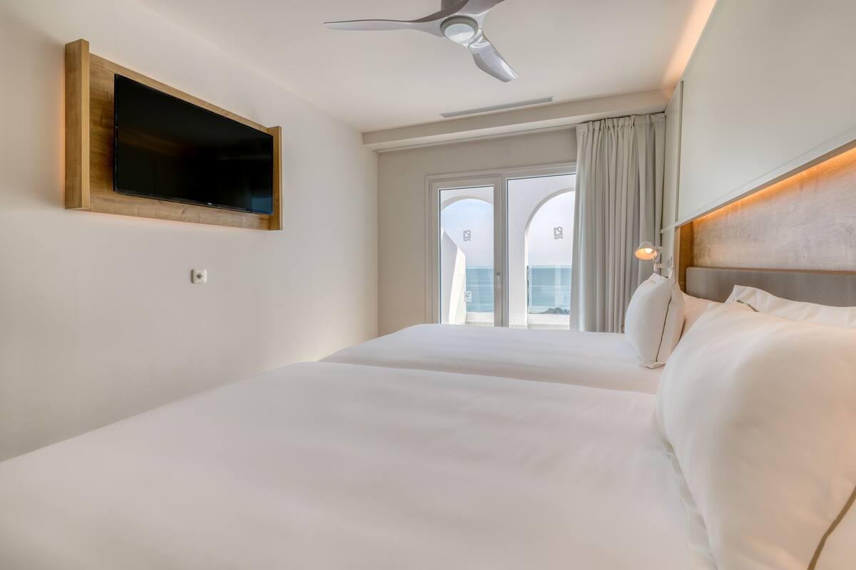 Une chambre d’hôtel dotée d’un grand lit, d’un ventilateur de plafond, d’un téléviseur fixé au mur et offrant une vue sur l’extérieur grâce à une grande fenêtre.