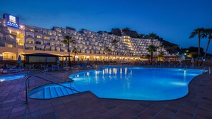 Un hôtel doté d’une piscine, de chaises longues et de palmiers.