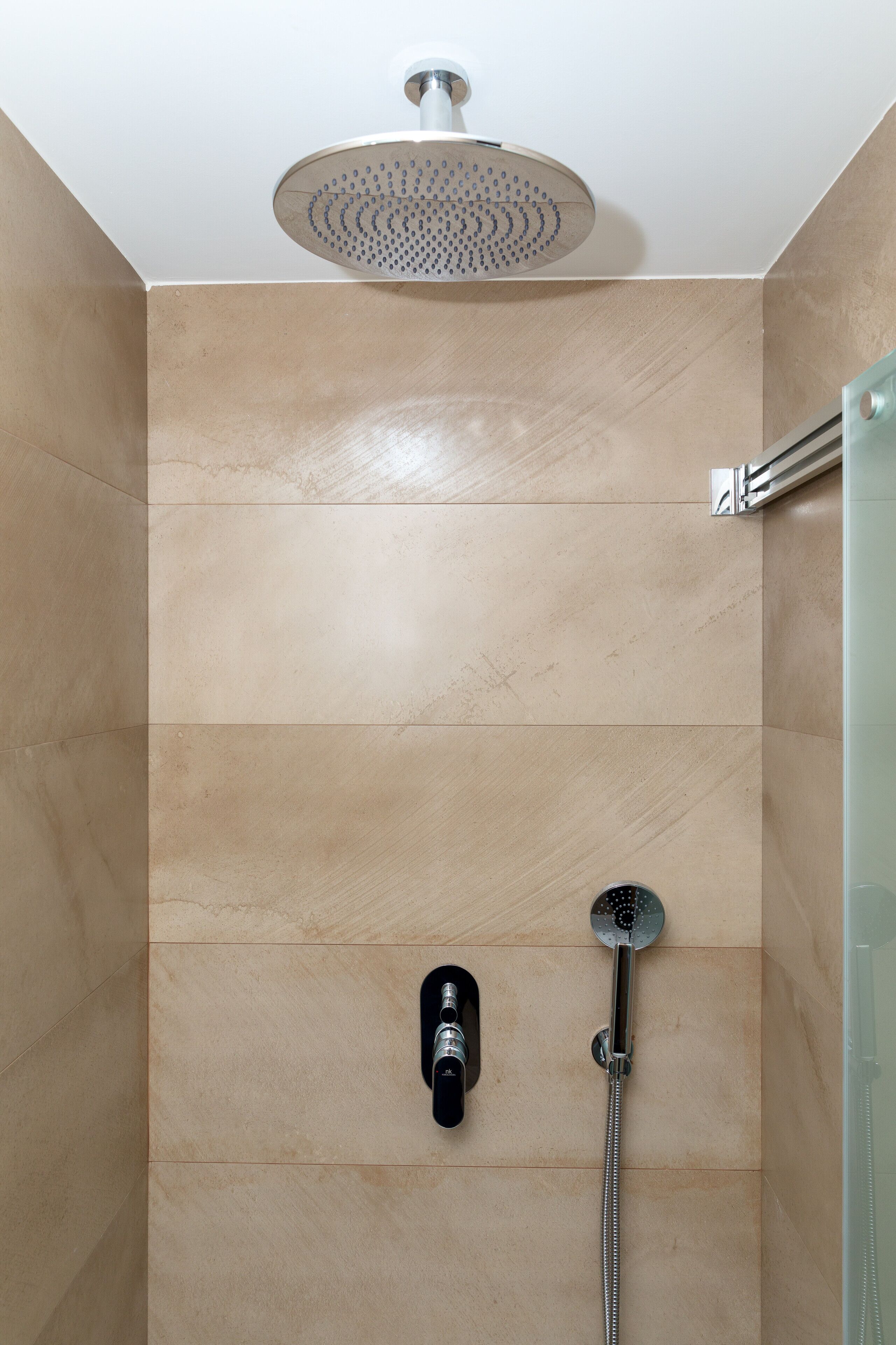 A modern shower area with a rain showerhead and a handheld showerhead mounted on the wall.
