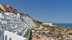 Een kusthotel met witte architectuur, een parkeerplaats en uitzicht op zee.