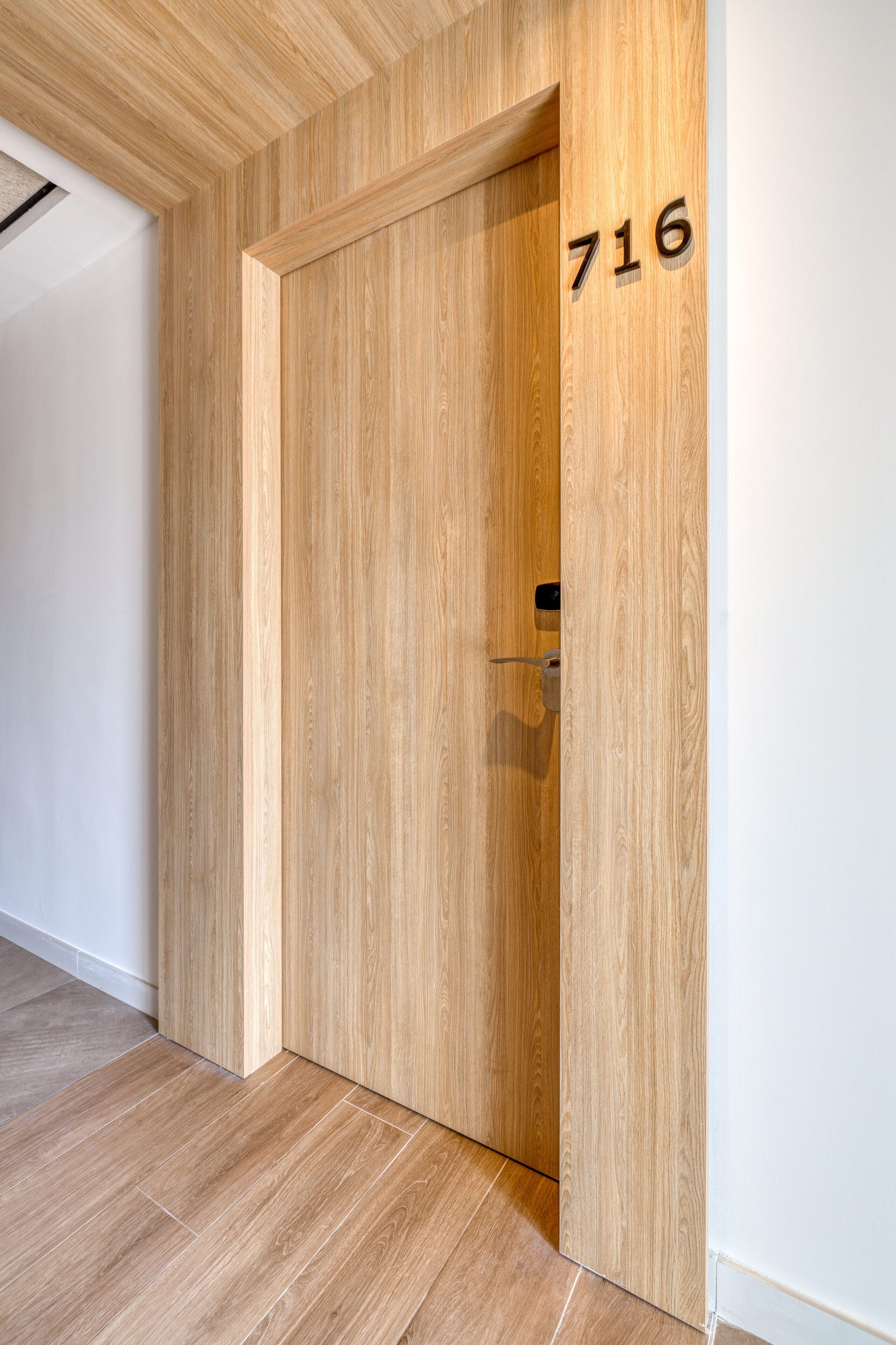 Una puerta de madera con el número 716, un interior moderno con suelo de madera y un techo con diseño de paneles de madera.
