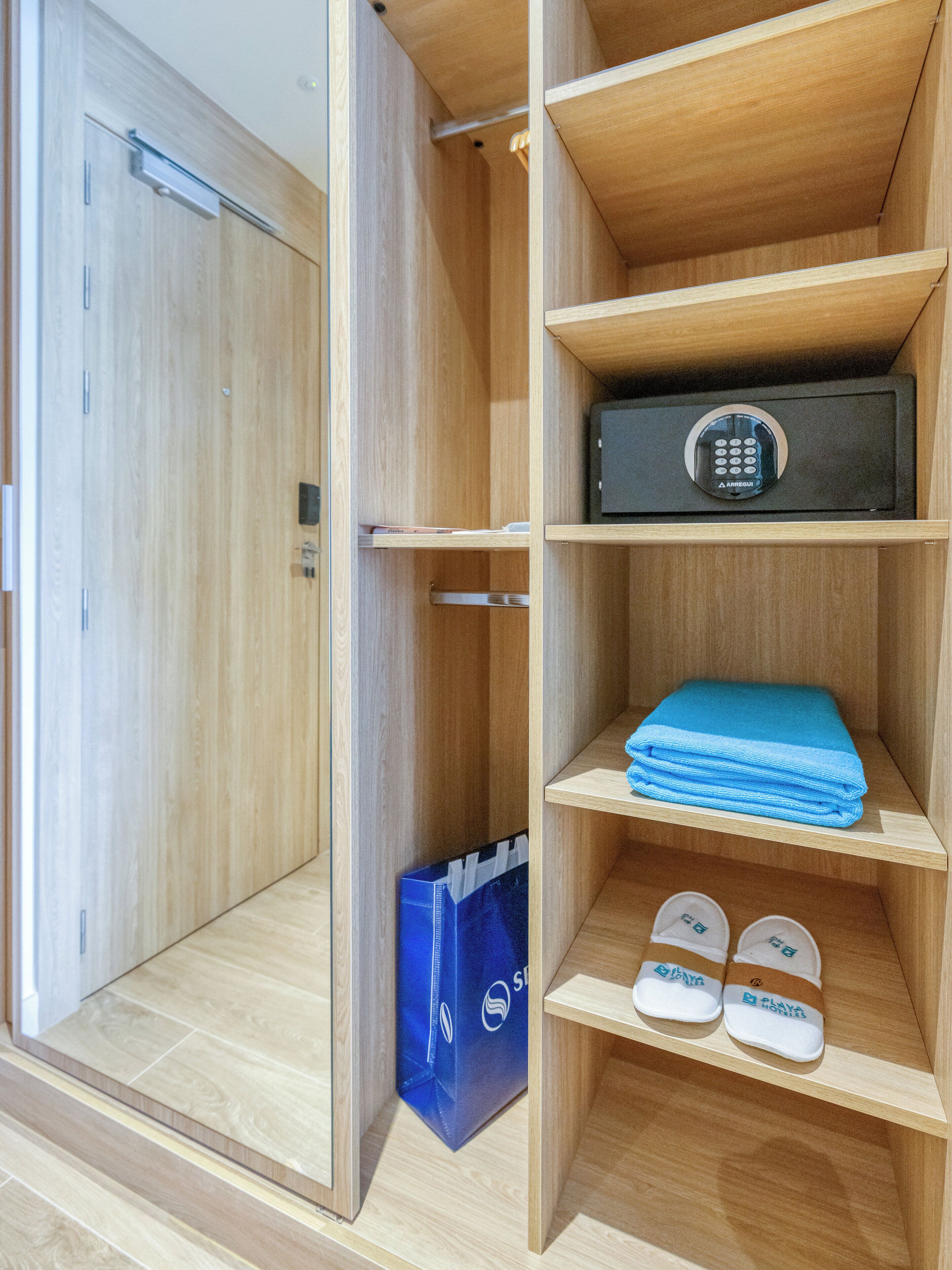 A wooden wardrobe with a built-in safe, a folded blue towel, and a pair of slippers.