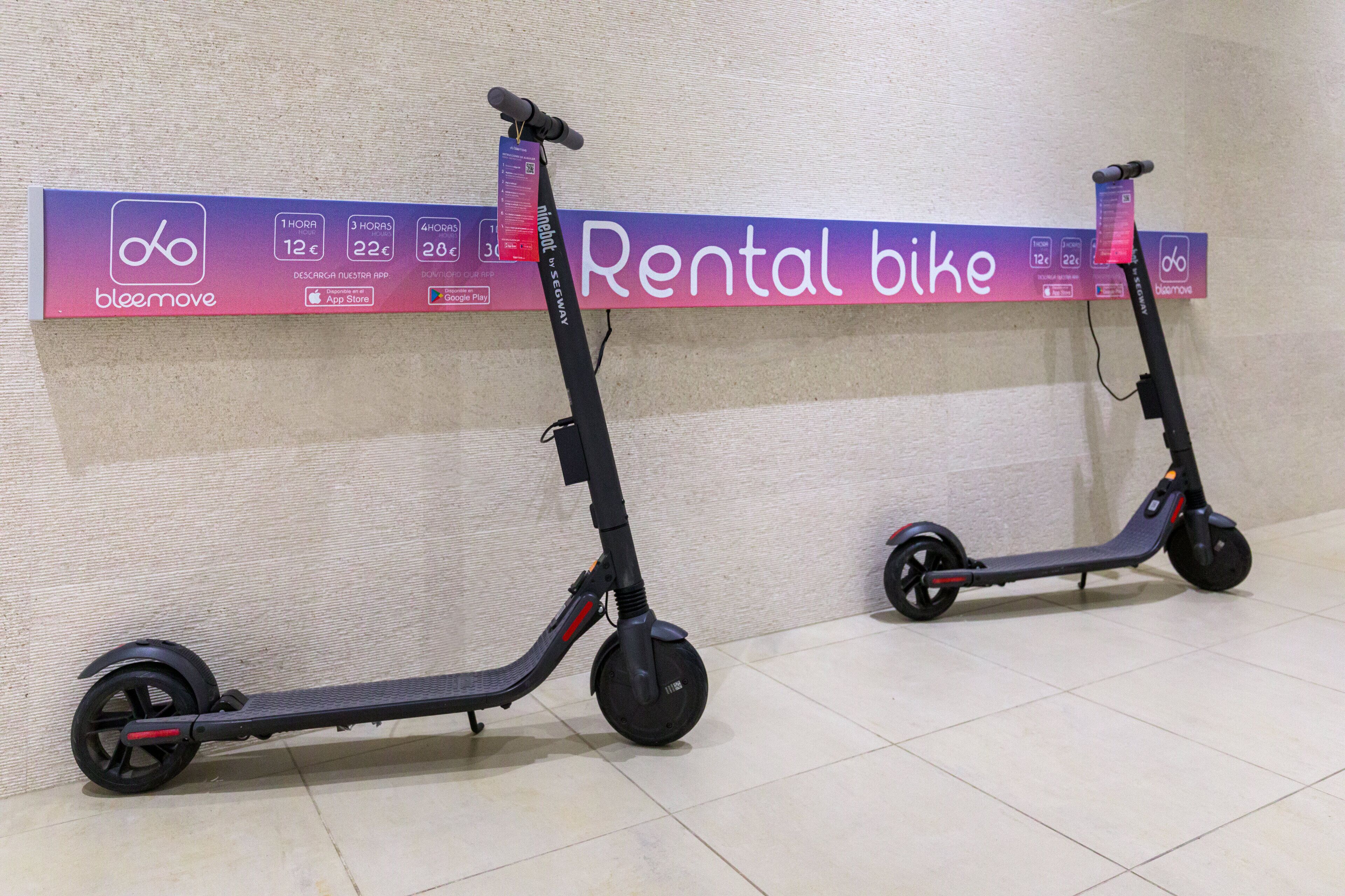 Dos bicicletas de alquiler con un letrero al fondo que anuncia un servicio de alquiler.