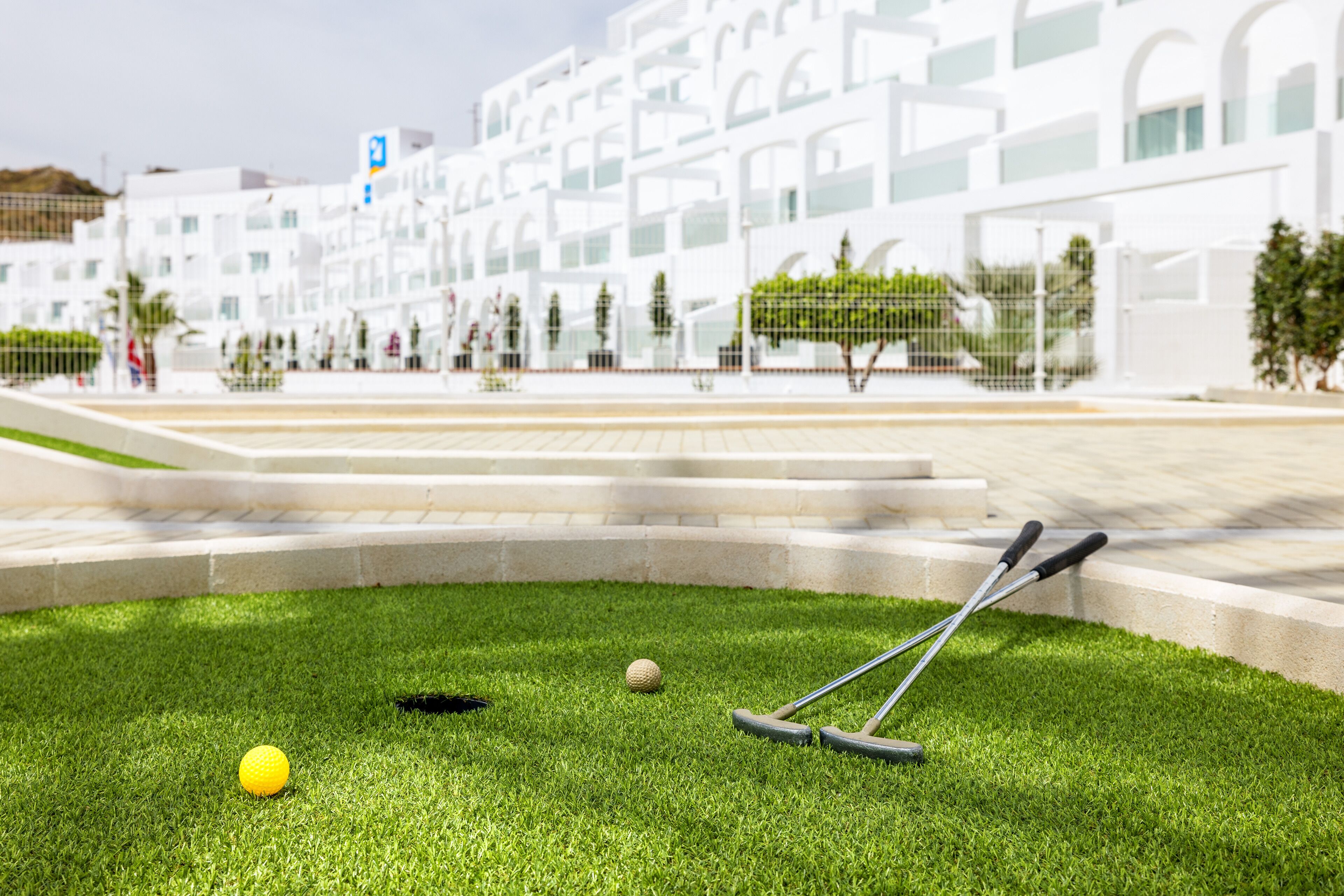 Un juego de croquet sobre un césped cuidado, con un edificio moderno al fondo.
