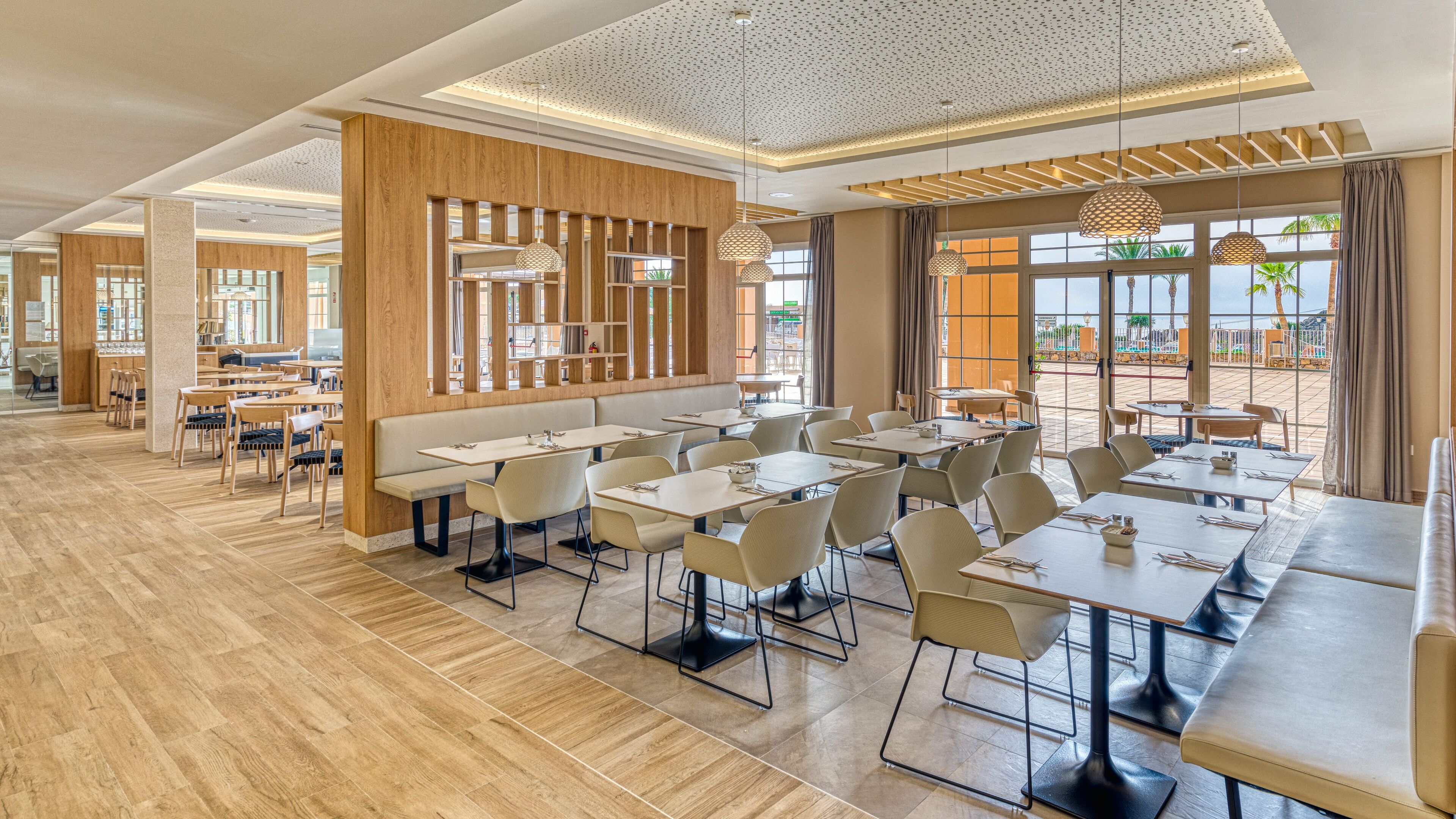 Een ruime eetruimte met houten lambrisering, modern meubilair en grote ramen met uitzicht op de omgeving.