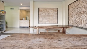 A reception area with a wooden bench, a refrigerator, and a wall-mounted floral carving. - RedDoorz @ Benesari 2 (Kuta)