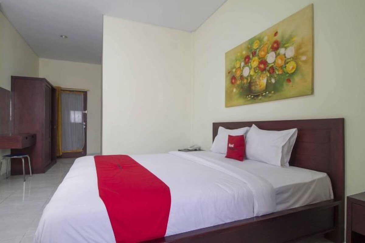 Une chambre d’hôtel avec un lit, un tableau représentant des fleurs accroché au mur, un bureau et une chaise.
