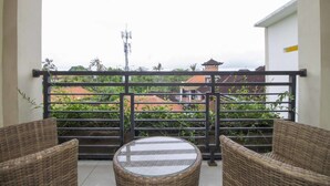 A balcony with wicker furniture and a glass table, overlooking a residential area with houses and greenery. - RedDoorz @ Benesari 2 (Kuta)
