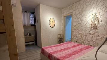 A bedroom with a bed, a clock, a stone wall, and a wooden door.