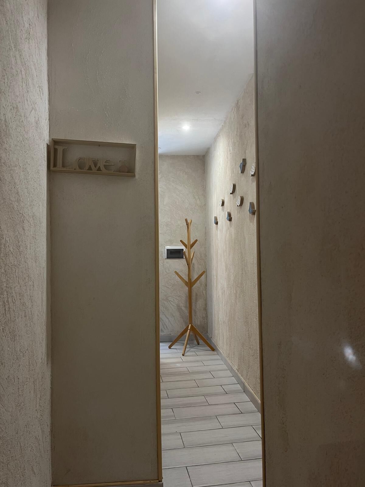 A hallway with a coat rack, a sign with the word "Love", and a wall-mounted thermostat.