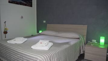 Un lit bien fait, avec une literie à rayures et des serviettes pliées, une table de chevet sur laquelle se trouve une lampe à lumière verte, et un tableau accroché au mur.