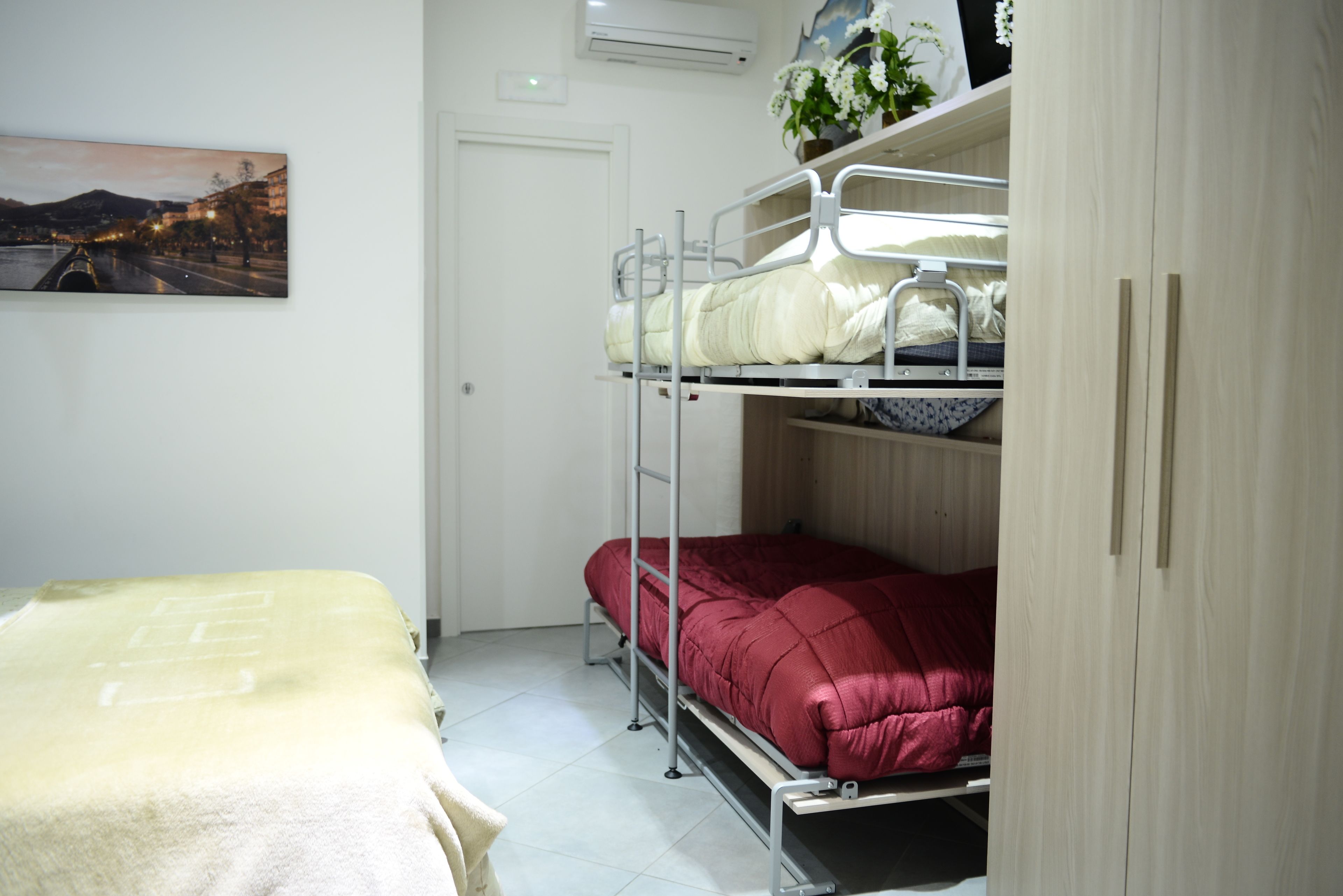 Une chambre de dortoir avec des lits superposés, un lit, un climatiseur fixé au mur et un tableau encadré accroché au mur.