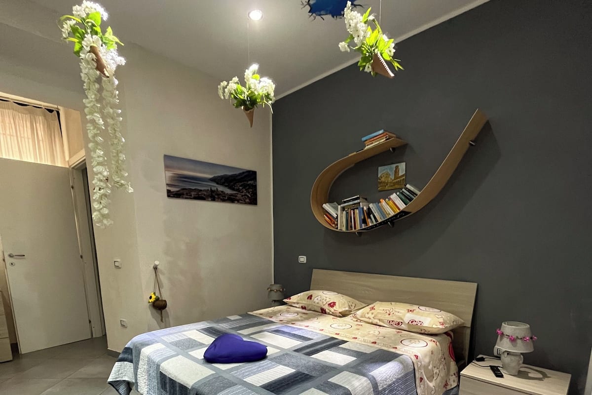 Une chambre à coucher comprenant un lit, des tables de chevet, une bibliothèque fixée au mur et des décorations florales suspendues.