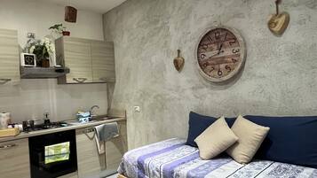 A modern bedroom with a bed, a wall clock, and a kitchen area.