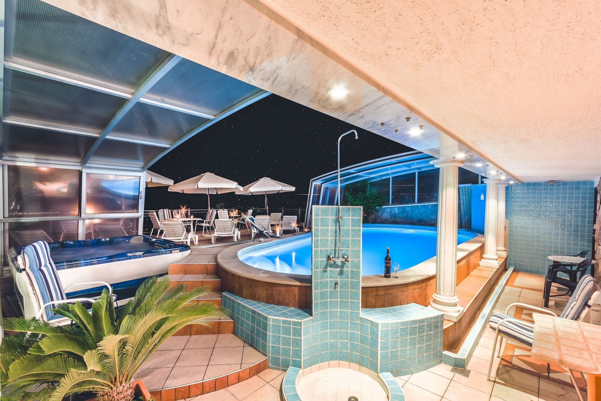 A luxurious indoor pool area with a hot tub, seating, and a view of the night sky.