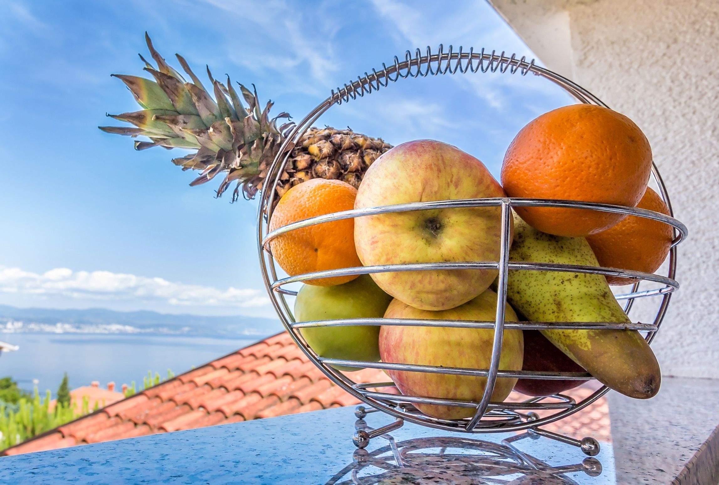 A fruit basket on a balcony with a view of the sea.