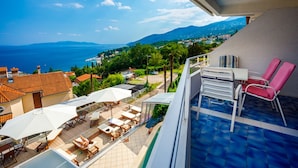 Ein Balkon mit Pool, Sitzgelegenheiten im Freien und Blick auf Meer und Berge.