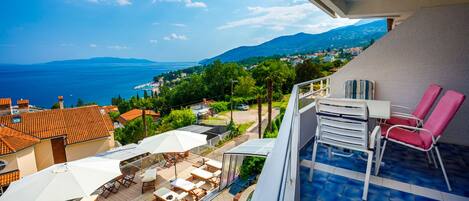 A balcony with a pool, outdoor seating, and a view of the sea and mountains.