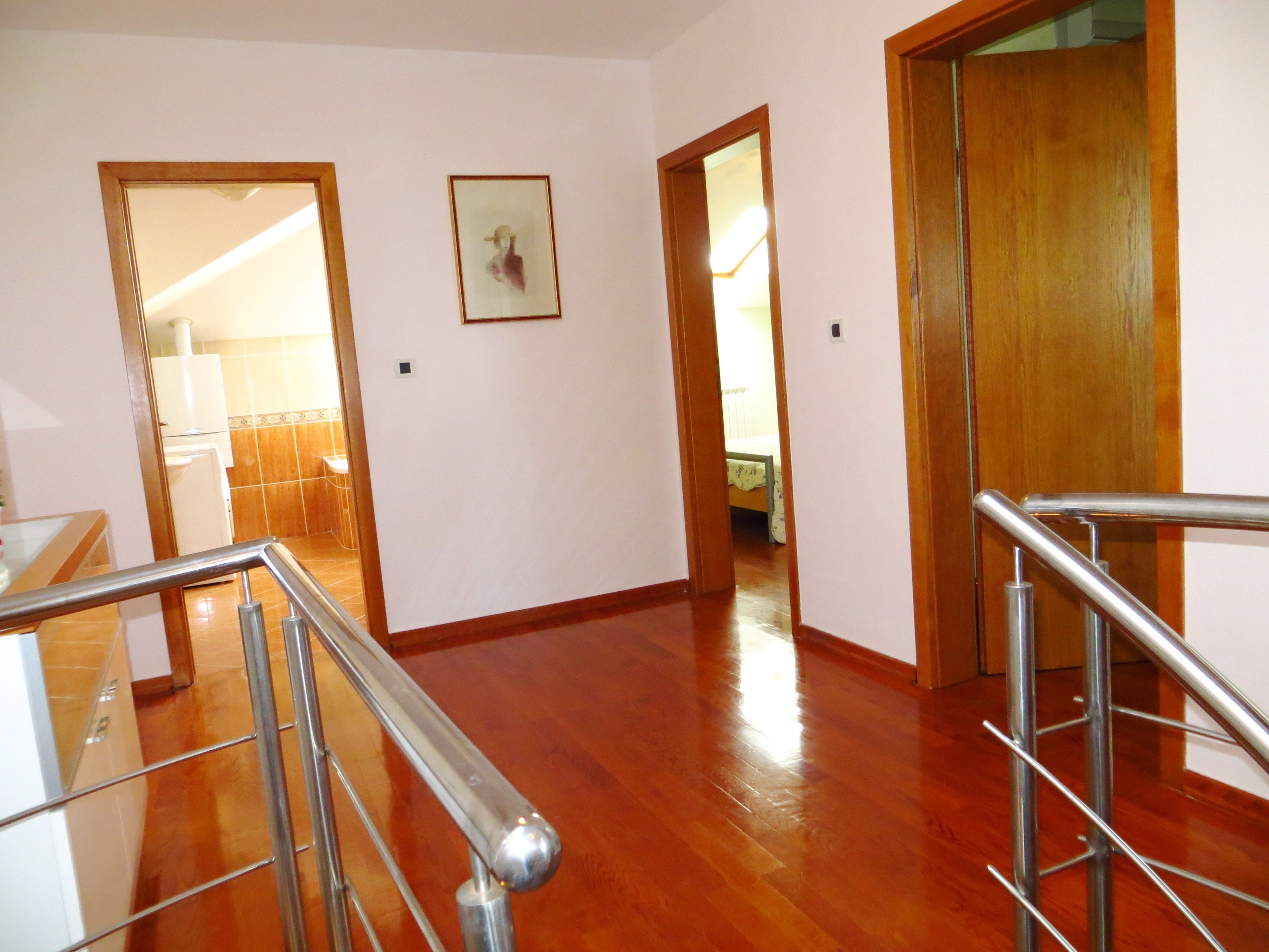 A hallway with wooden flooring, a staircase with metal railings, and a door leading to another room.