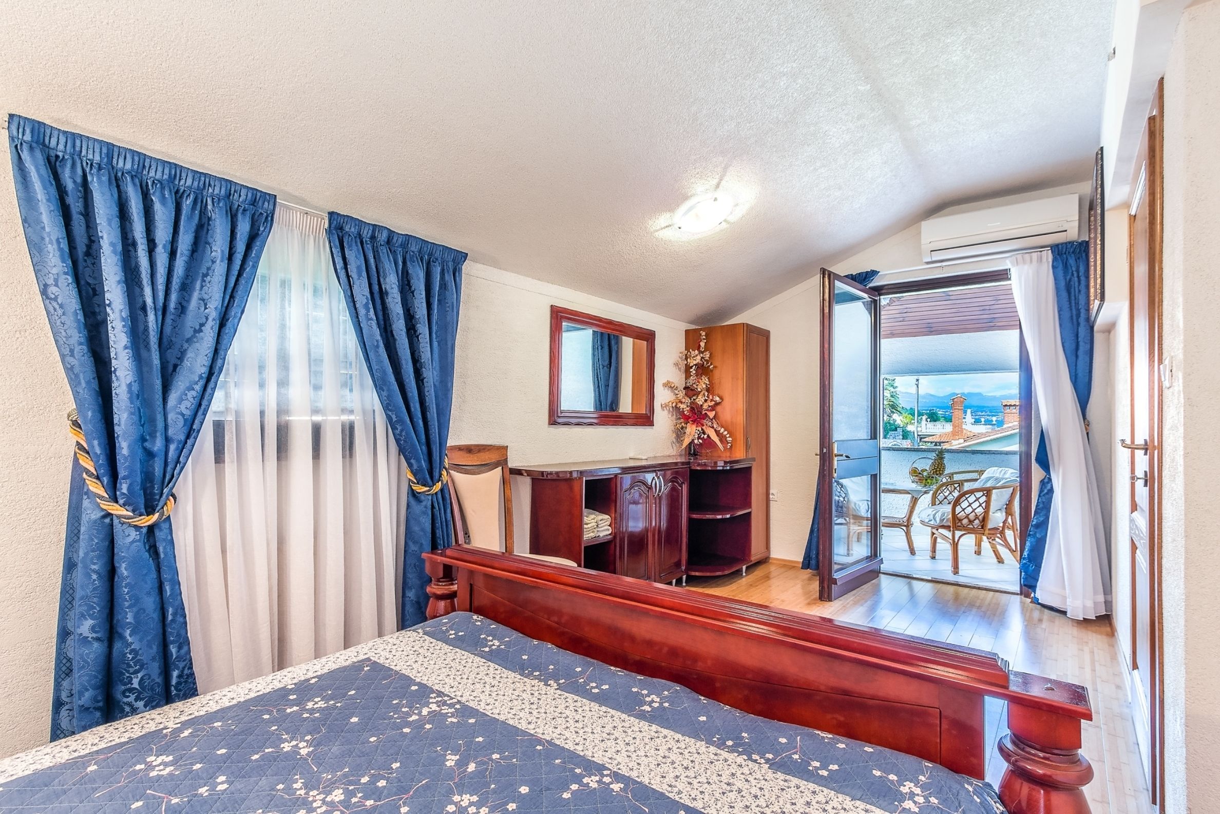 A bedroom with a bed, a dresser, a mirror, and a balcony with a view.