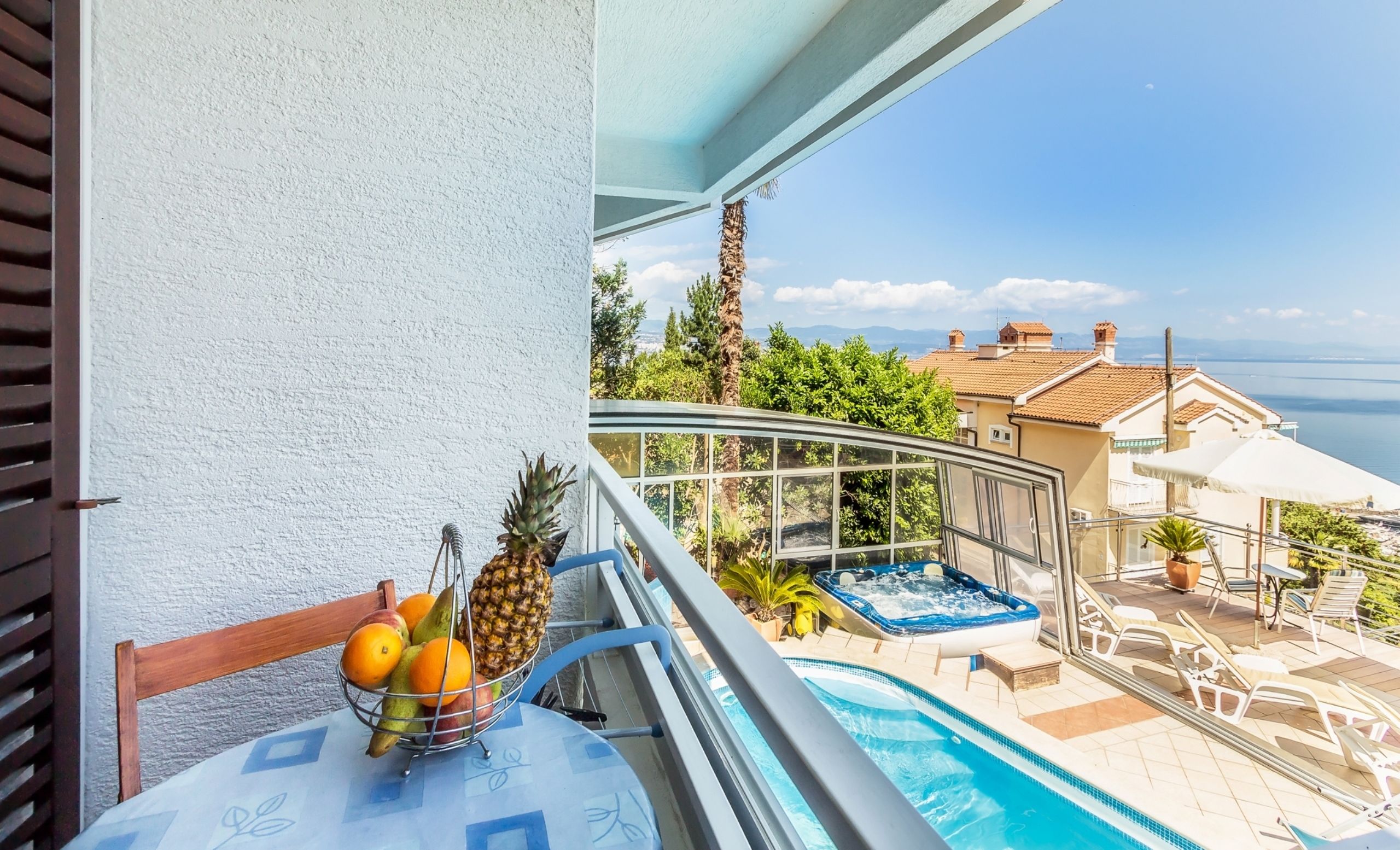Un balcón con piscina, una cesta de frutas y vistas al mar y edificios.