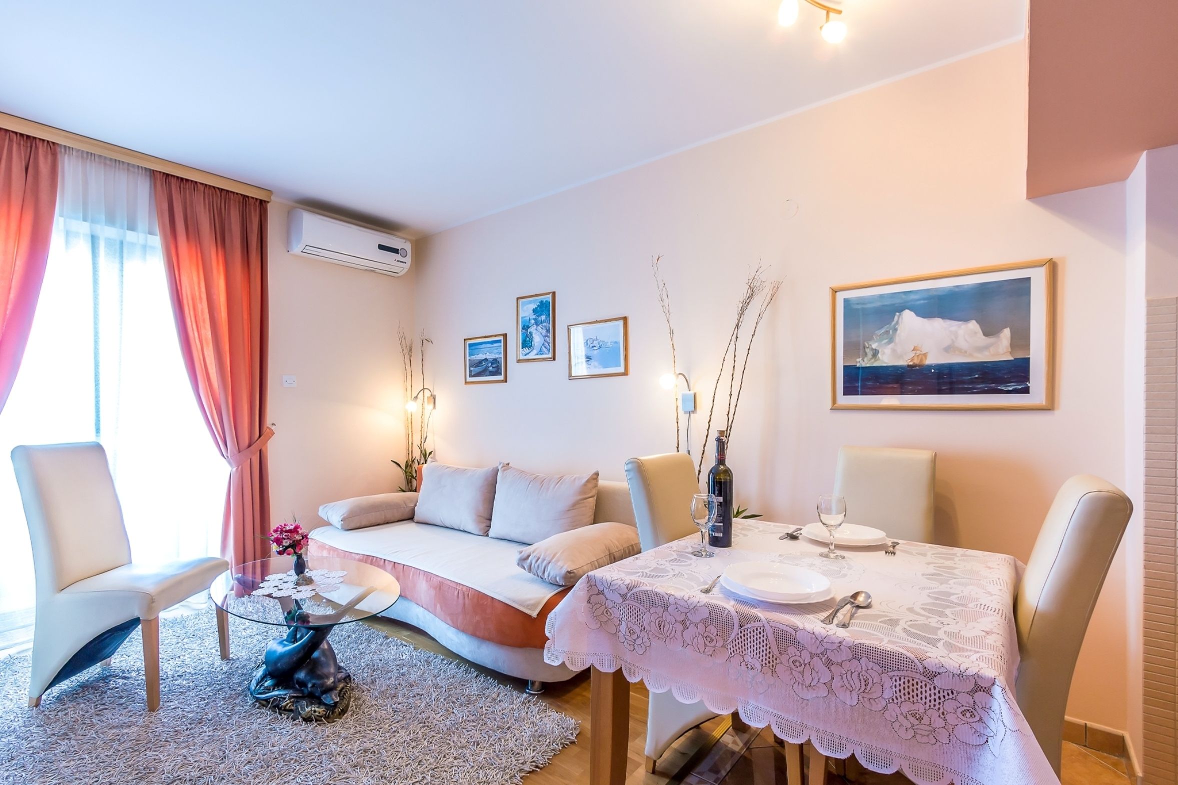 Un salon chaleureux avec un canapé, une table à manger recouverte d’une nappe en dentelle et un tableau représentant un iceberg.