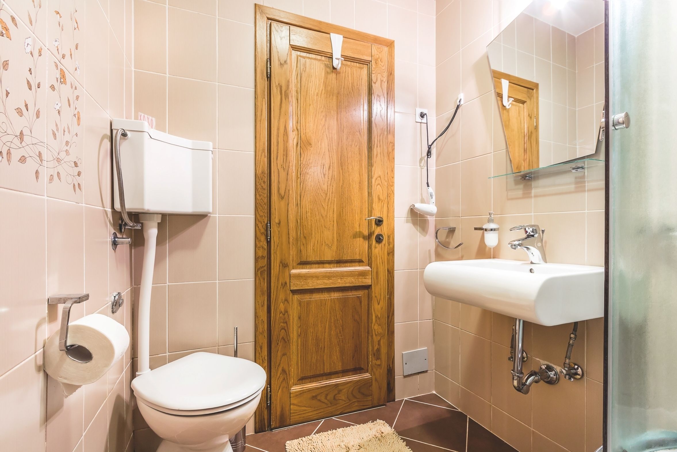 A bathroom with a toilet, a wooden door, a sink, and a mirror.