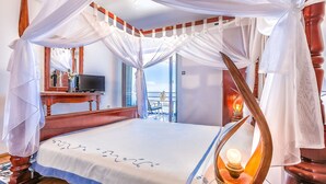 Ein Himmelbett mit weißer Bettdecke, eine Nachttischlampe und Blick auf den Balkon.