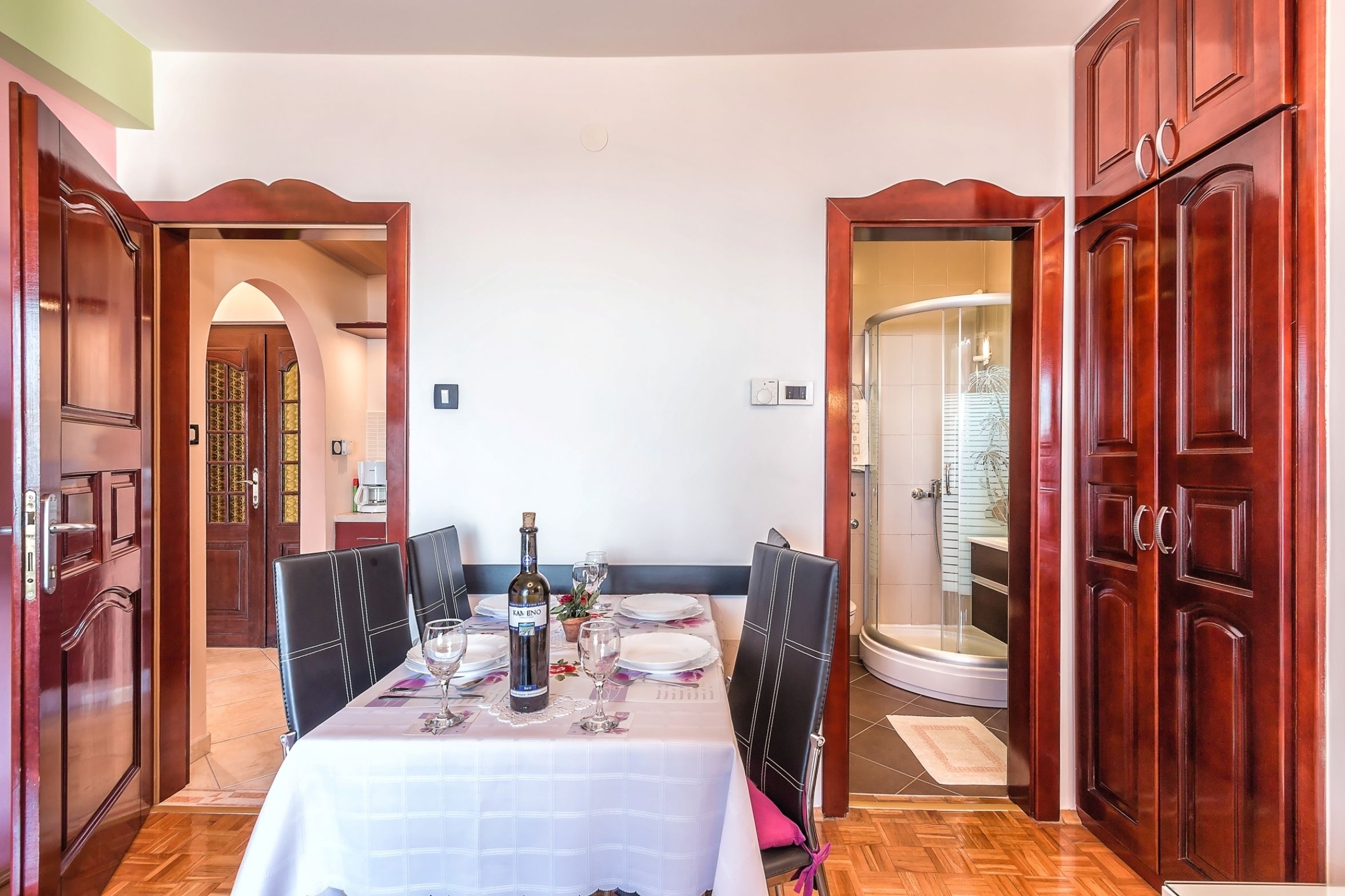 A dining area with a table set for four, a bottle of wine, and a shower visible through an open door.