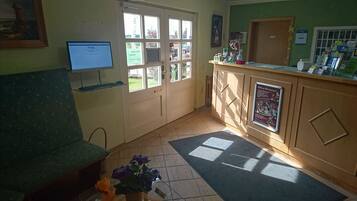 A reception area with a computer monitor, a green couch, a tiled floor, and a window with a view of greenery.