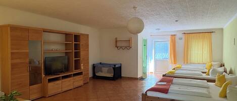 A room with a wooden TV stand, a sofa, a bed with multiple pillows, and a small table with a plant.