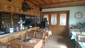 Un coin bar au style rustique, avec des meubles en bois, un comptoir où sont exposées différentes bouteilles et différents verres, et un espace détente avec des tables et des chaises.