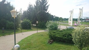 Un chemin pavé mène à une zone herbeuse où se trouvent un lampadaire et une poubelle en métal.