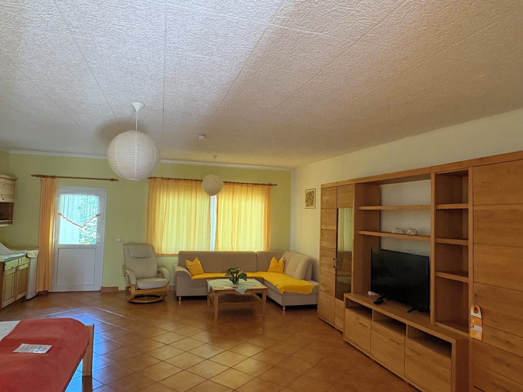 A living room with a sofa, armchair, coffee table, TV stand, and a dining area with a table and chairs.