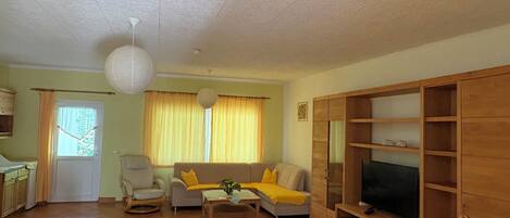 A living room with a sofa, armchair, coffee table, TV stand, and a dining area with a table and chairs.