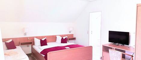 A hotel room with a bed, a desk with a TV, a chair, and a small table with flowers.