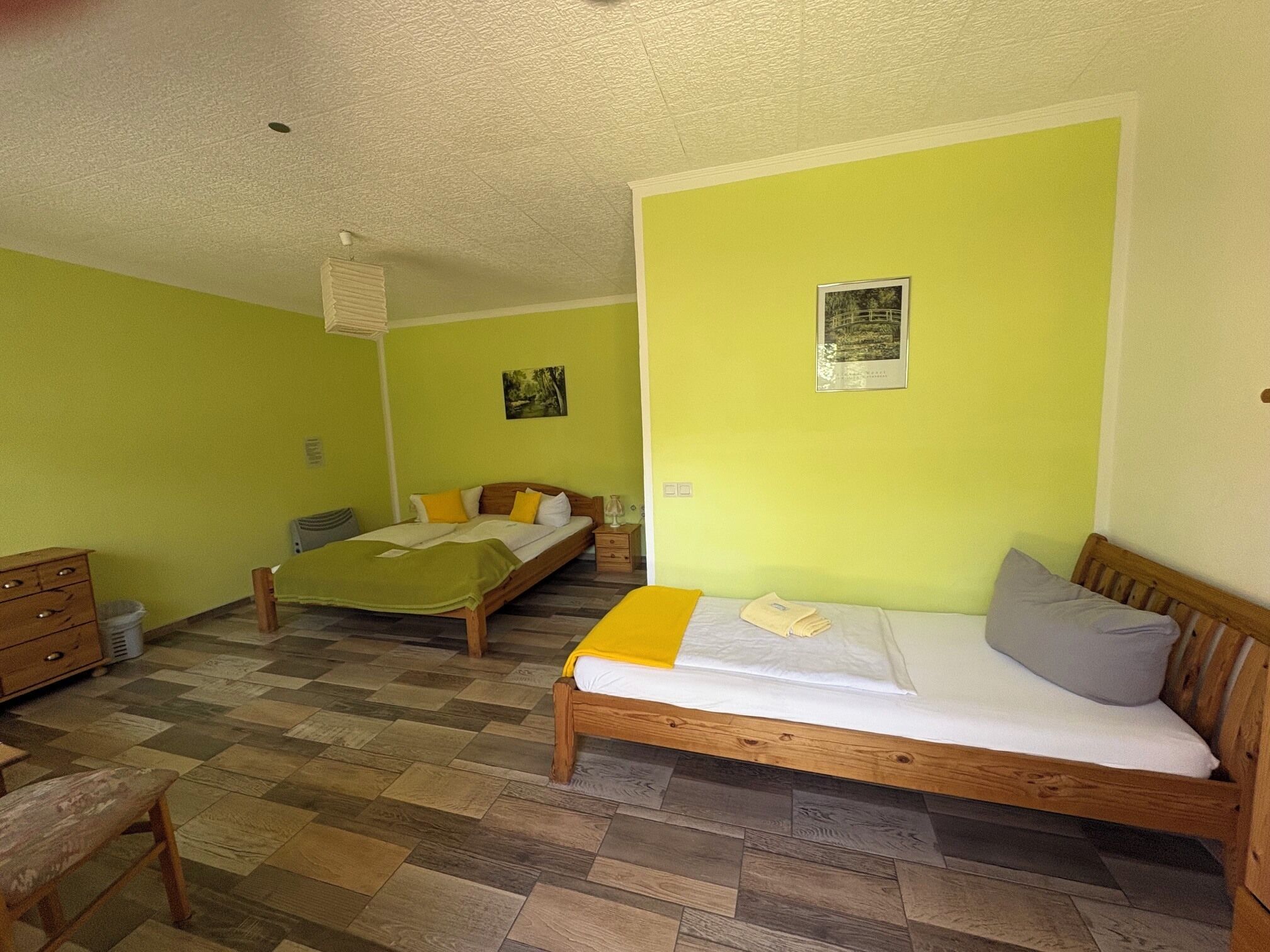 A room with two wooden beds, a wooden bench, a small wooden dresser, and a tiled floor.
