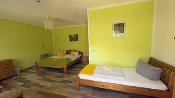A room with two wooden beds, a wooden bench, a small wooden dresser, and a tiled floor.